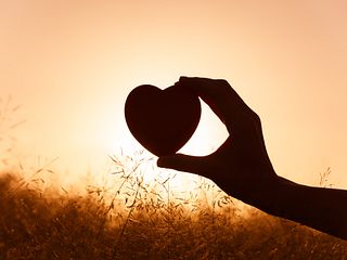Hand holding heart against beautiful setting.
