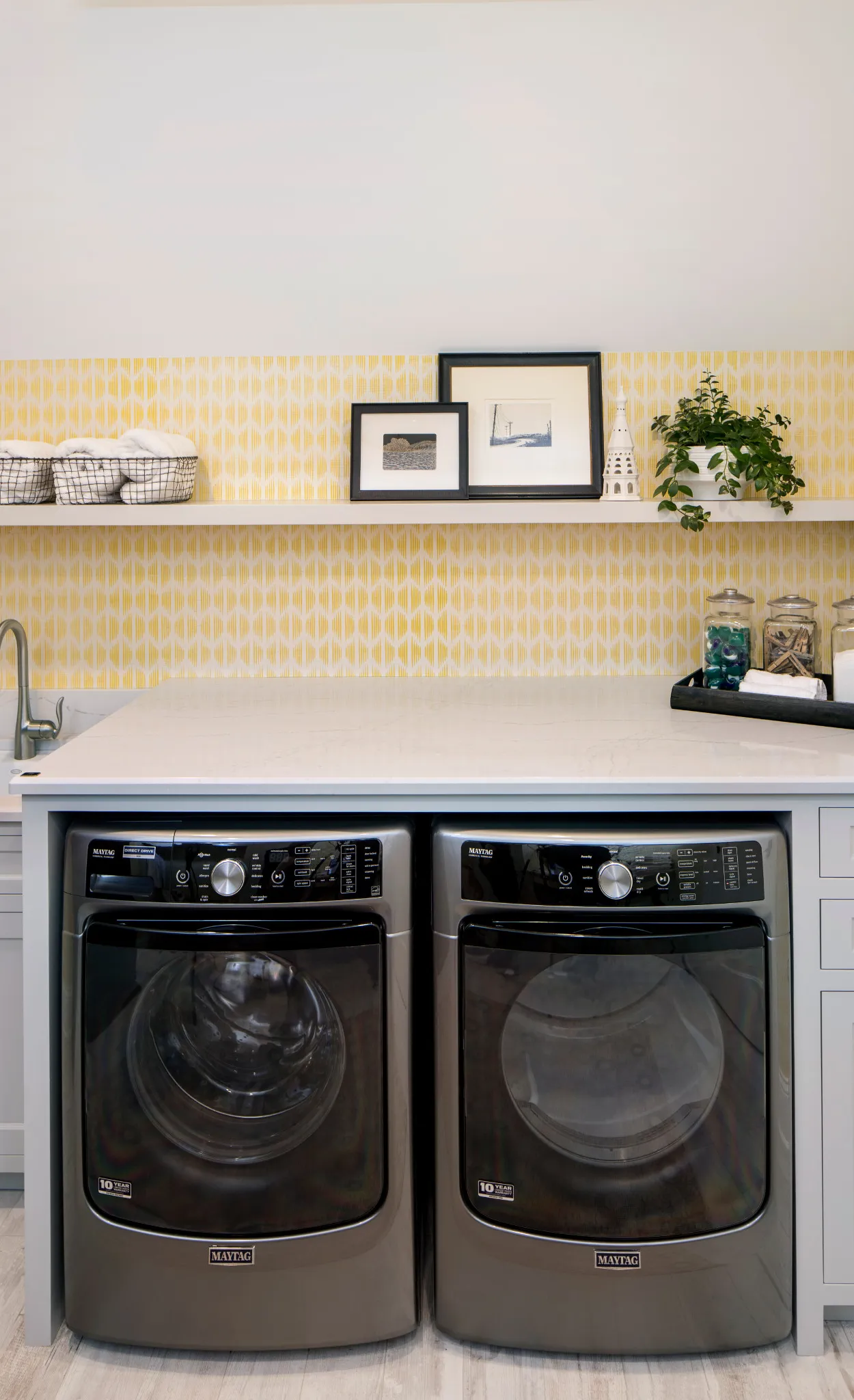 a cheerful laundry room with yellow wallpaper, Cambria Ella quartz countertops, open shelving, and a washer and dryer.