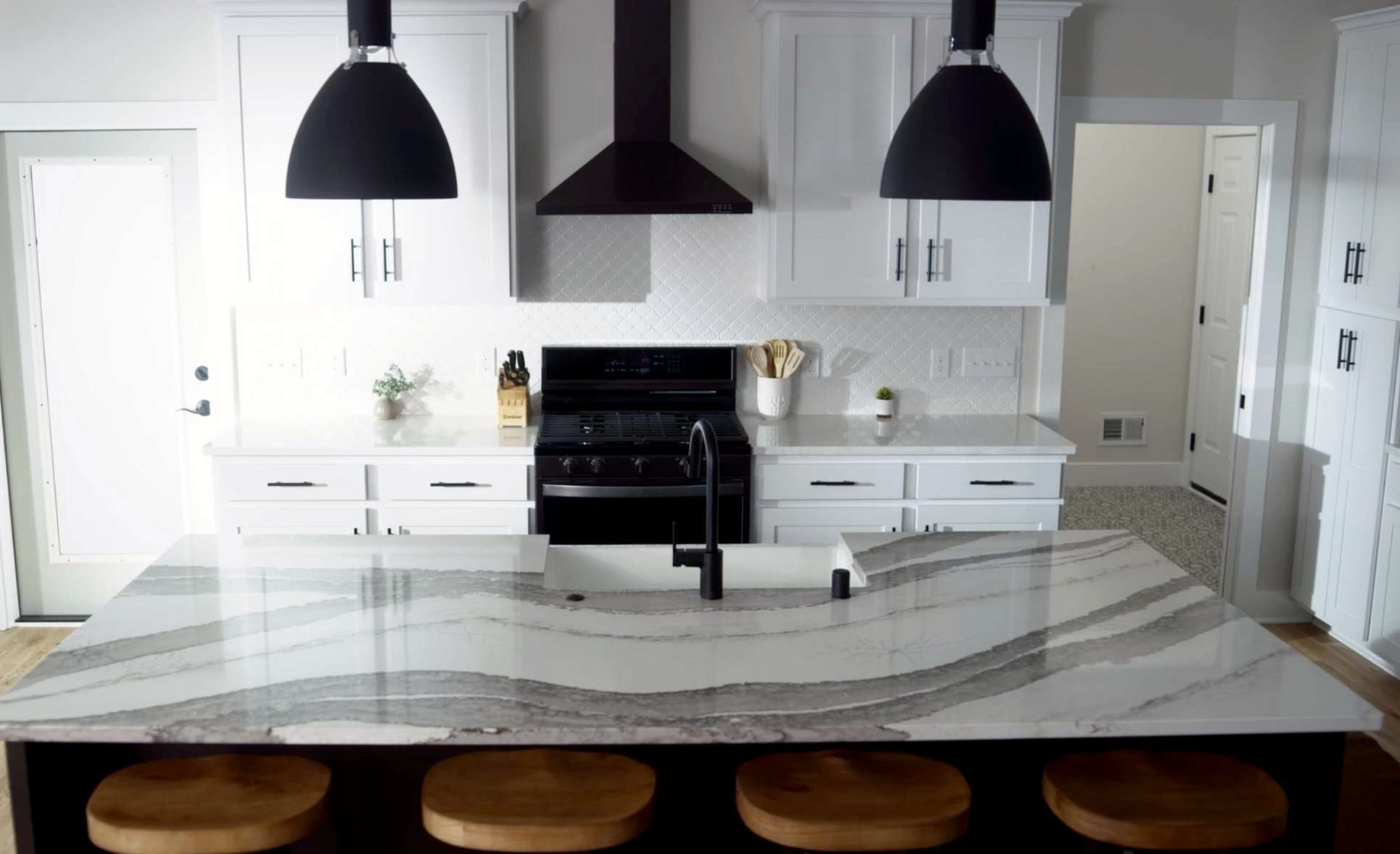 A white kitchen features Cambria Skara Brae and Ironsbridge with black appliances and lighting.