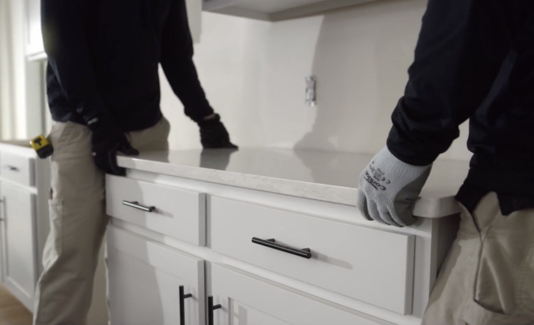 Two installers place a Cambria countertop onto a white cabinet for install.