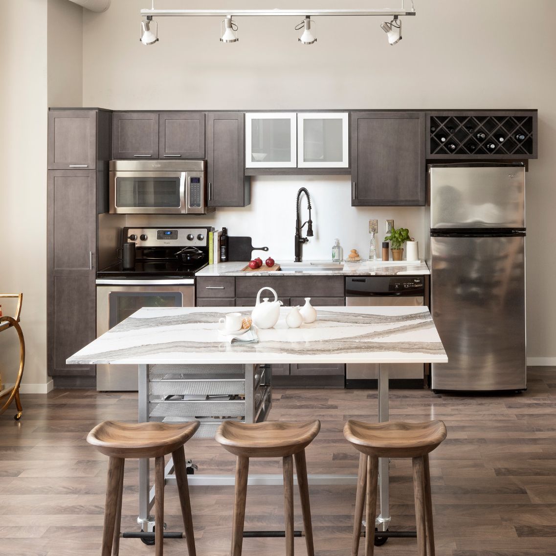 A sleek warm toned kitchen with brown cabinets and a mobile metal island with Cambria Skara Brae countertops.
