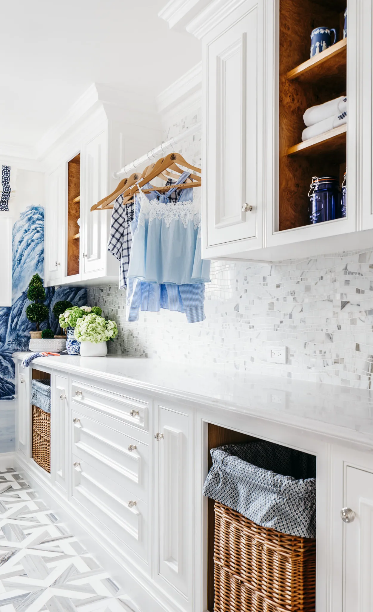 a blue and white themed laundry room featuring Cambria Ella quartz countertops, shelving, and two built-in laundry hampers with a geometric tile backsplash.