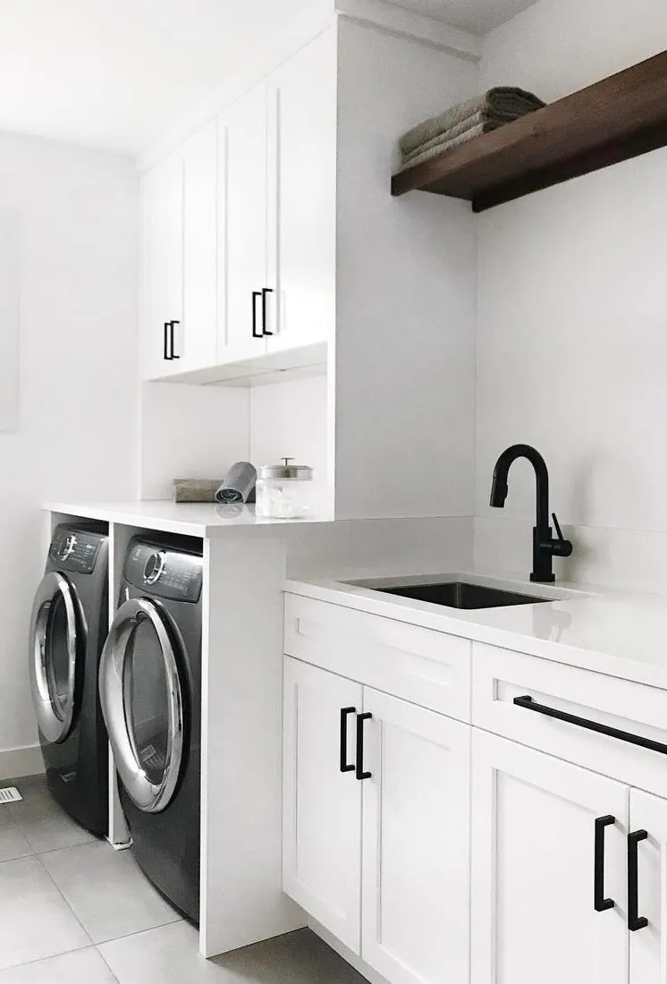 a crisp white laundry room with Cambria Quartz White Cliff countertops, white cabinetry, open wood shelving, and a black sink.
