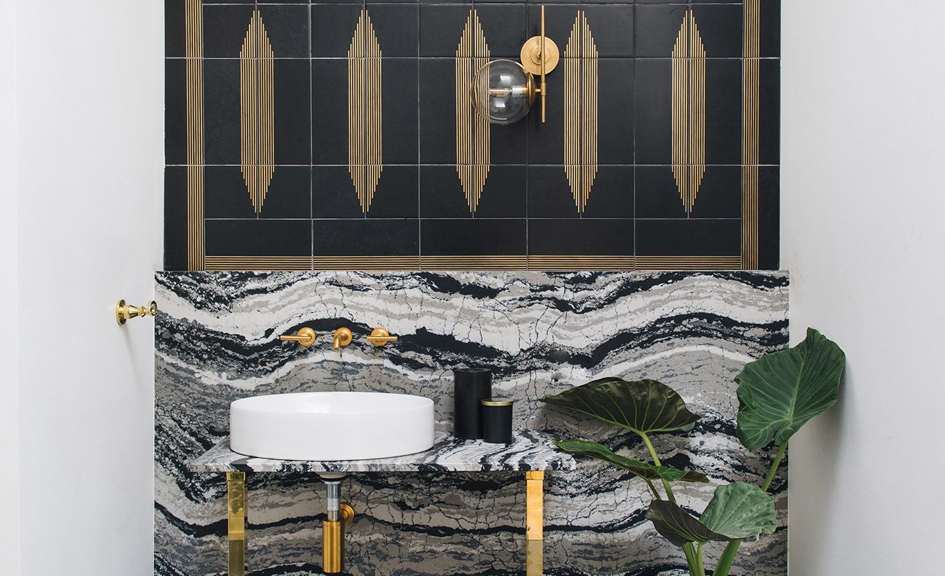 A Cambria Levven™ backsplash and vanity pairs with matte black and brass in this studio bathroom .