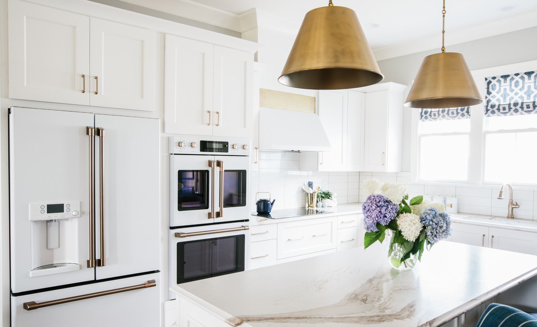 Cambria Brittanicca Gold in a white kitchen with coordinating white appliances and gold pendant lighting.