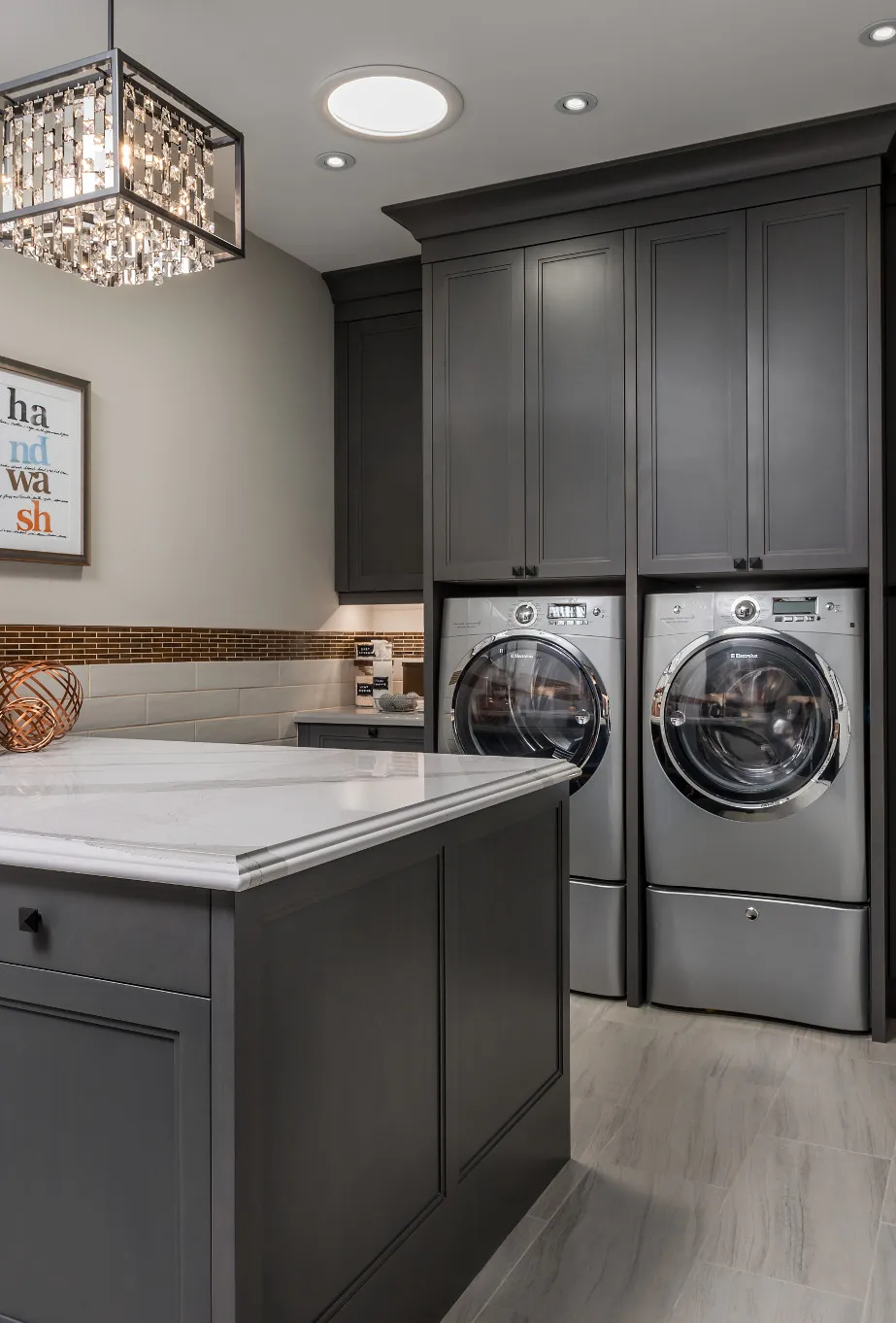 a gray laundry room with a washer and dryer and a center island topped with Cambria Brittanicca quartz countetops.