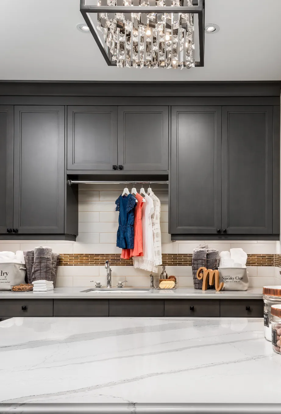 a gray laundry room with a center island topped with Cambria Brittanicca quartz countetops and open shelving to hang clothes.