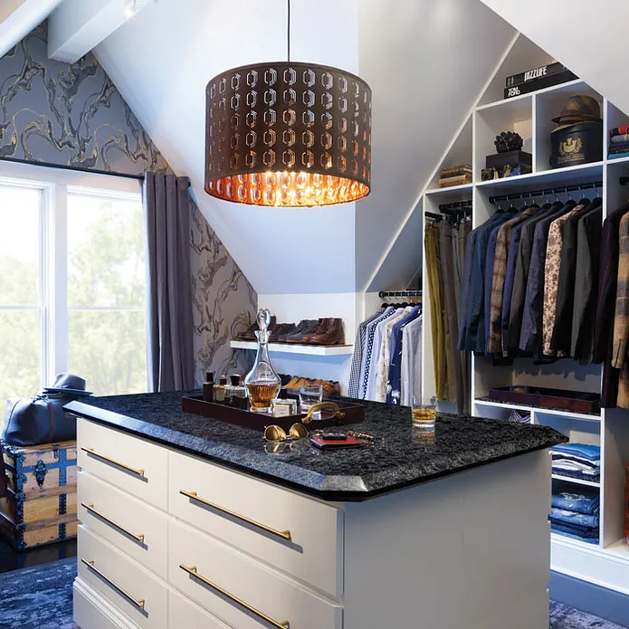 a men's closet with an island featuring Cambria Sharpham quartz countertops, a large chandelier over the island, blue carpet and patterned wallpaper, and open shelving to hang clothes.