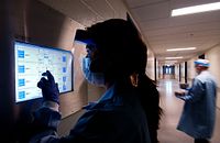 Lab technician looking at a computer screen wearing a lab coat and face mask.