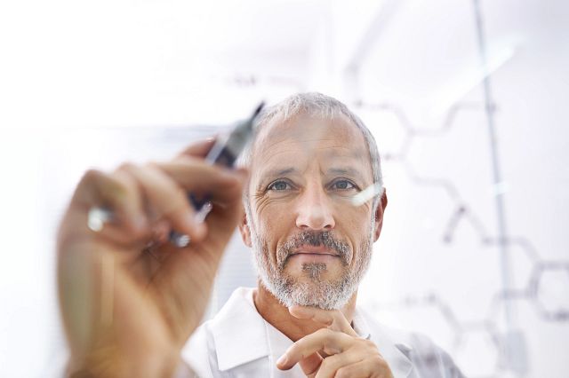 Scientist draws molecular structures on a glass surface to help show the parent drug and the associated metabolite identification.