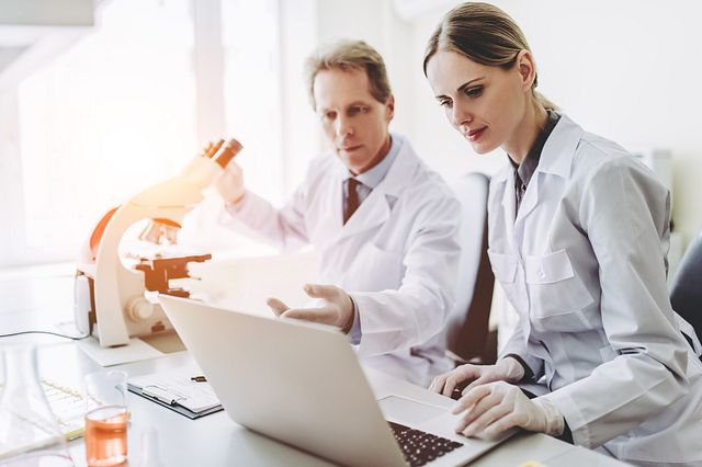 Two scientists wearing white coats working together.