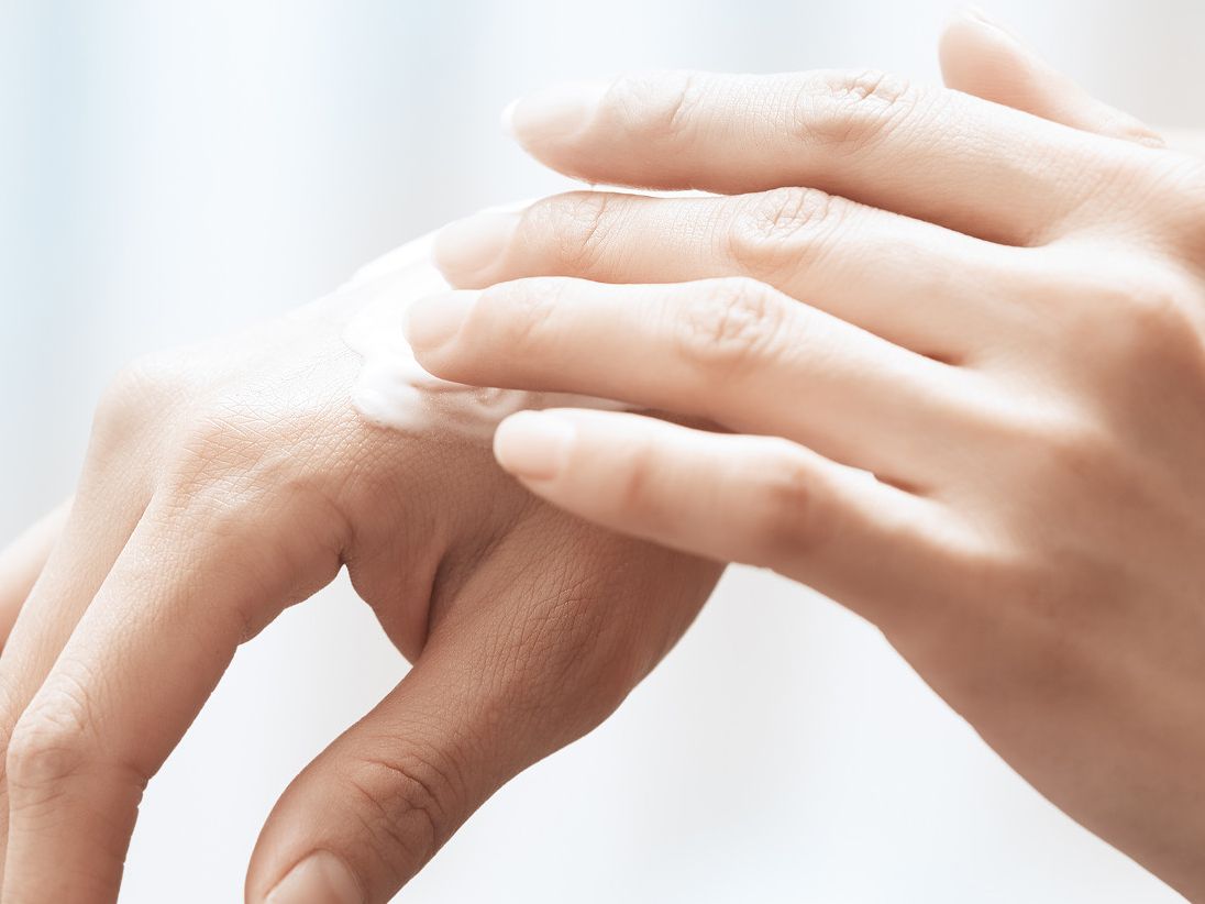 Hands rubbing medication on skin inflammation.