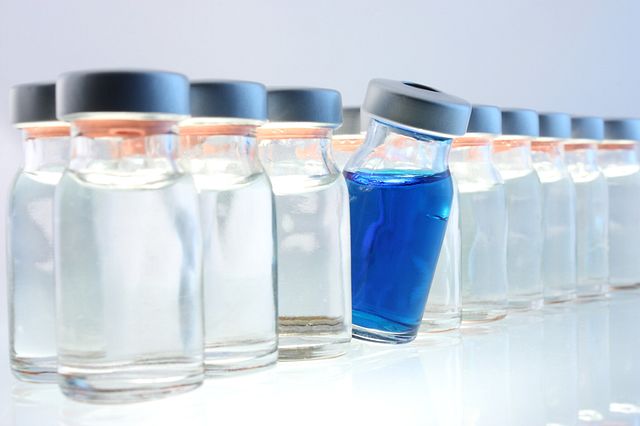 row of medical vials with clear liquid and one with blue liquid