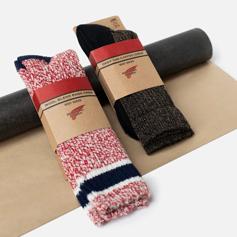 Two pairs of socks laying on a roll of leather against a white background