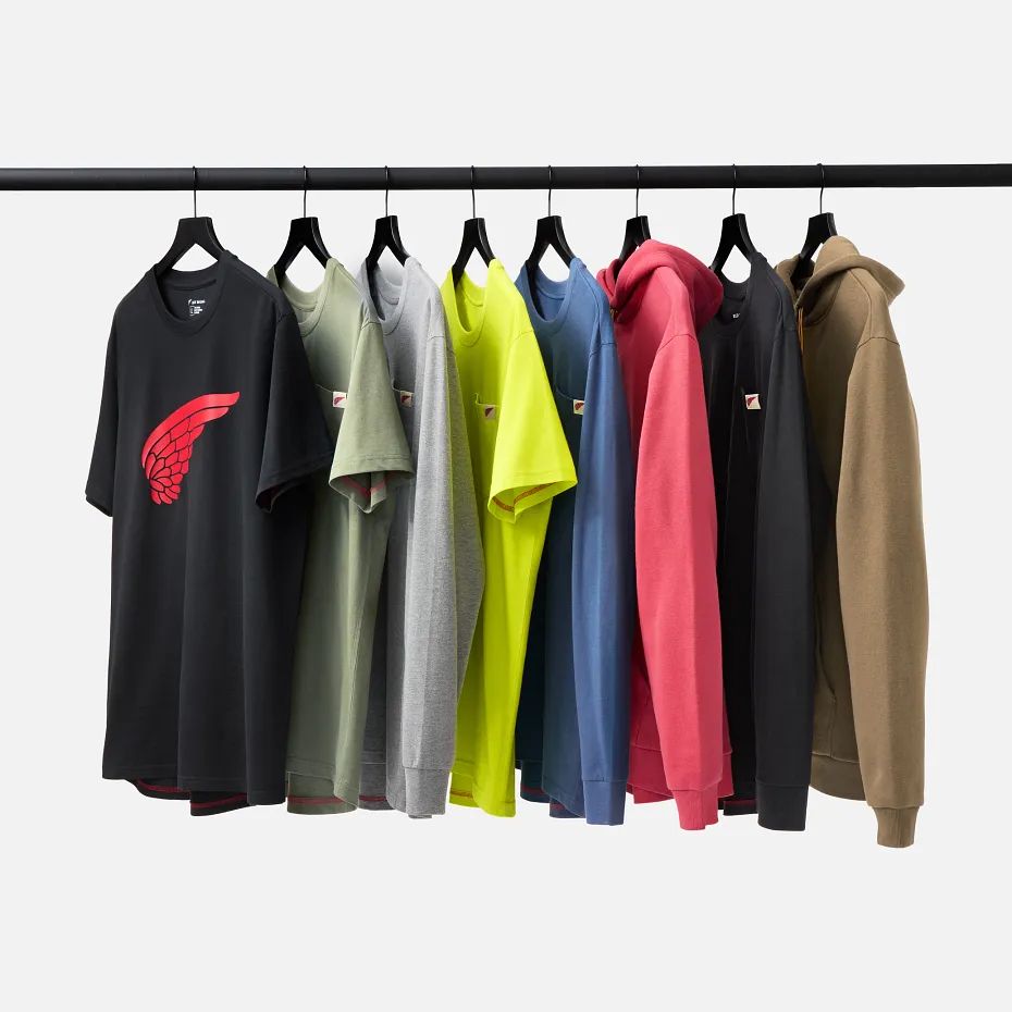 Several shirts and sweatshirts hanging on hangers on a pole against a white background