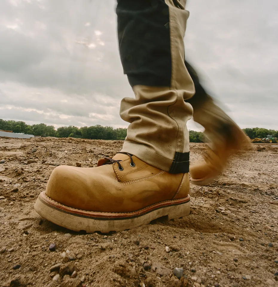 Close up of a person's leg and boot walking on gravel