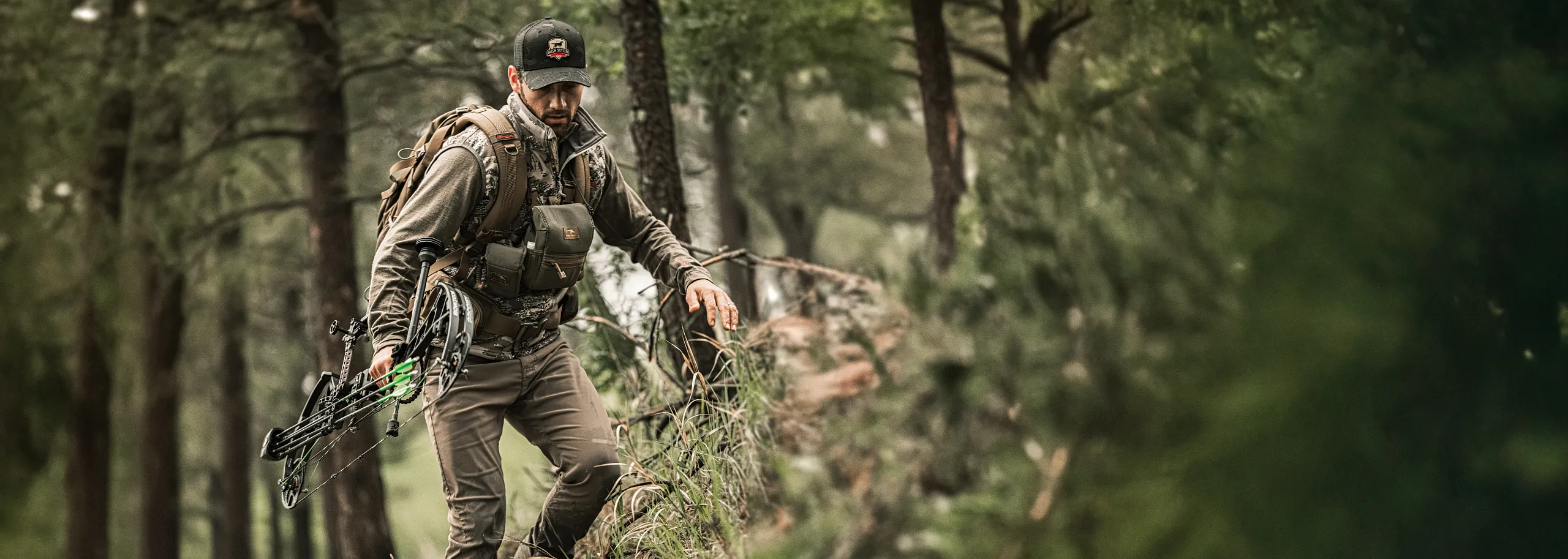 A man with a bow and hunting gear walking through the woods