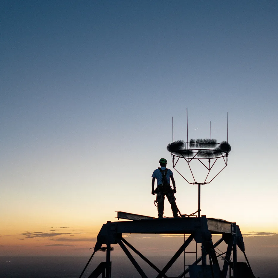 A man standing on a tall tower with the sun setting on the horizon