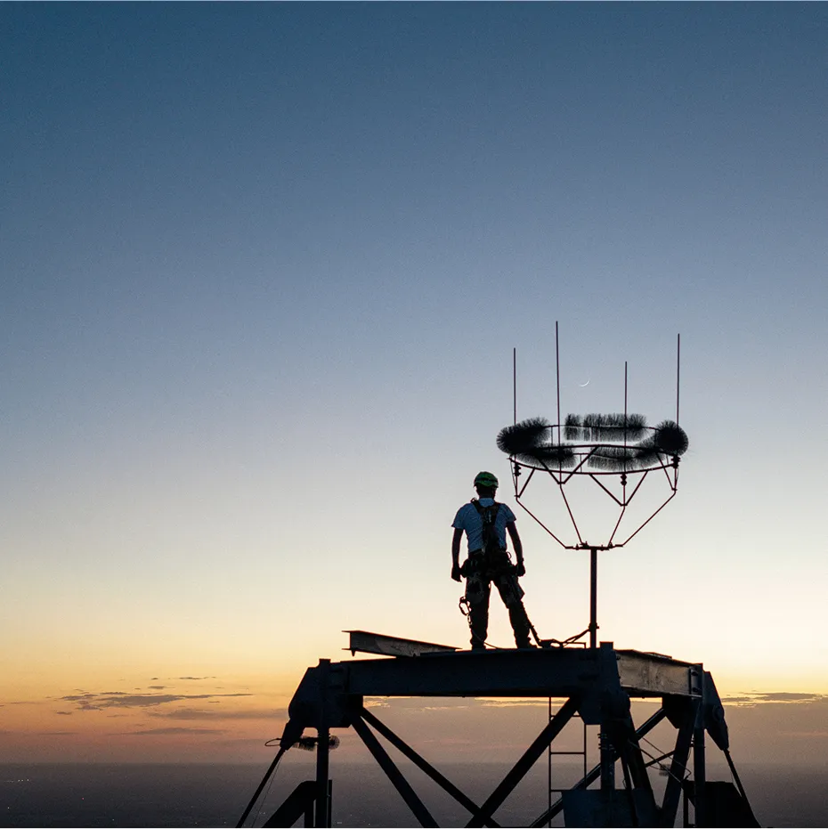 A man standing on a tall tower with the sun setting on the horizon