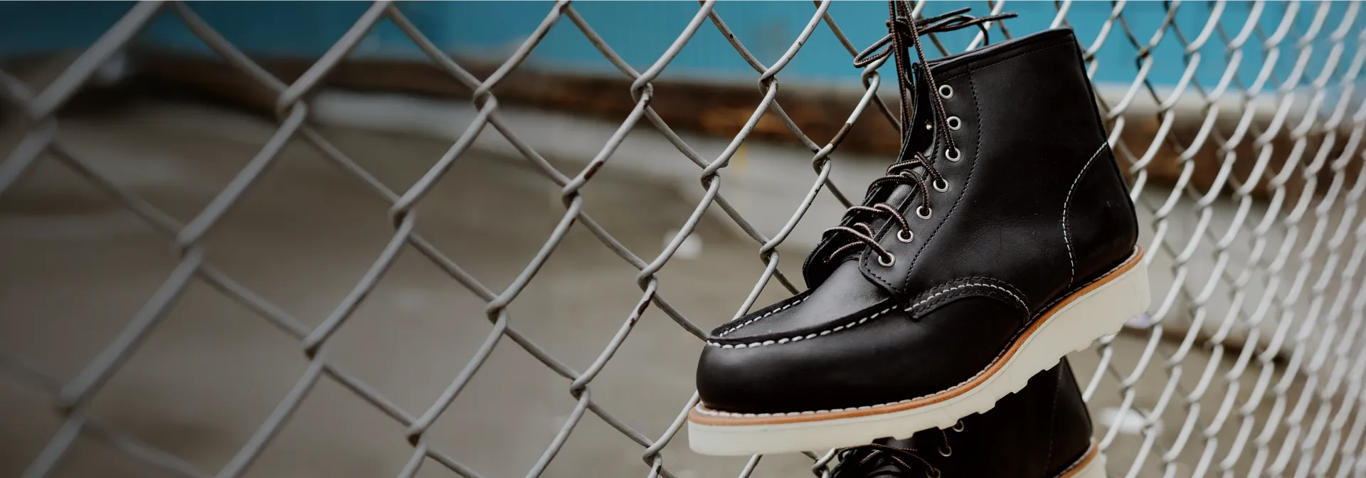 A pair of black boots hanging by the laces on a chain link fence