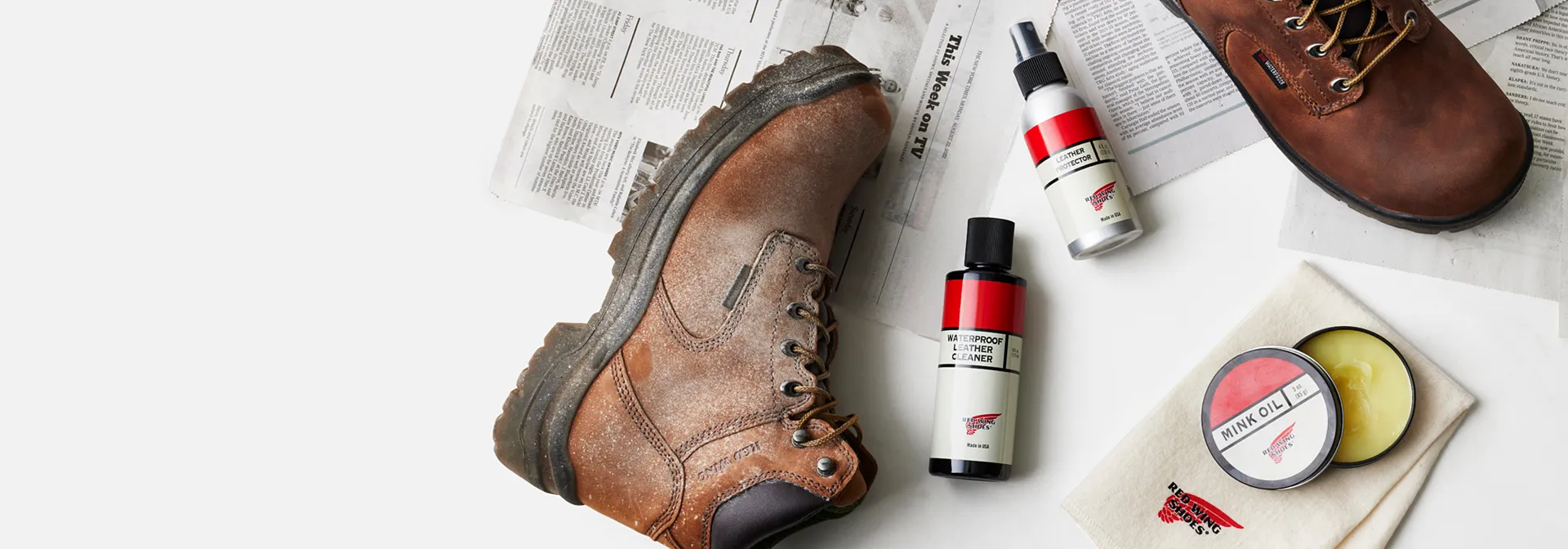 Overhead view of a pair of boots and several boot care products laying on newspaper against a white background