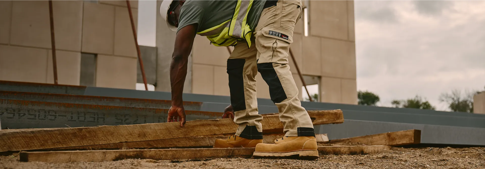 Man at a construction site in workwear bending over to pick up a board