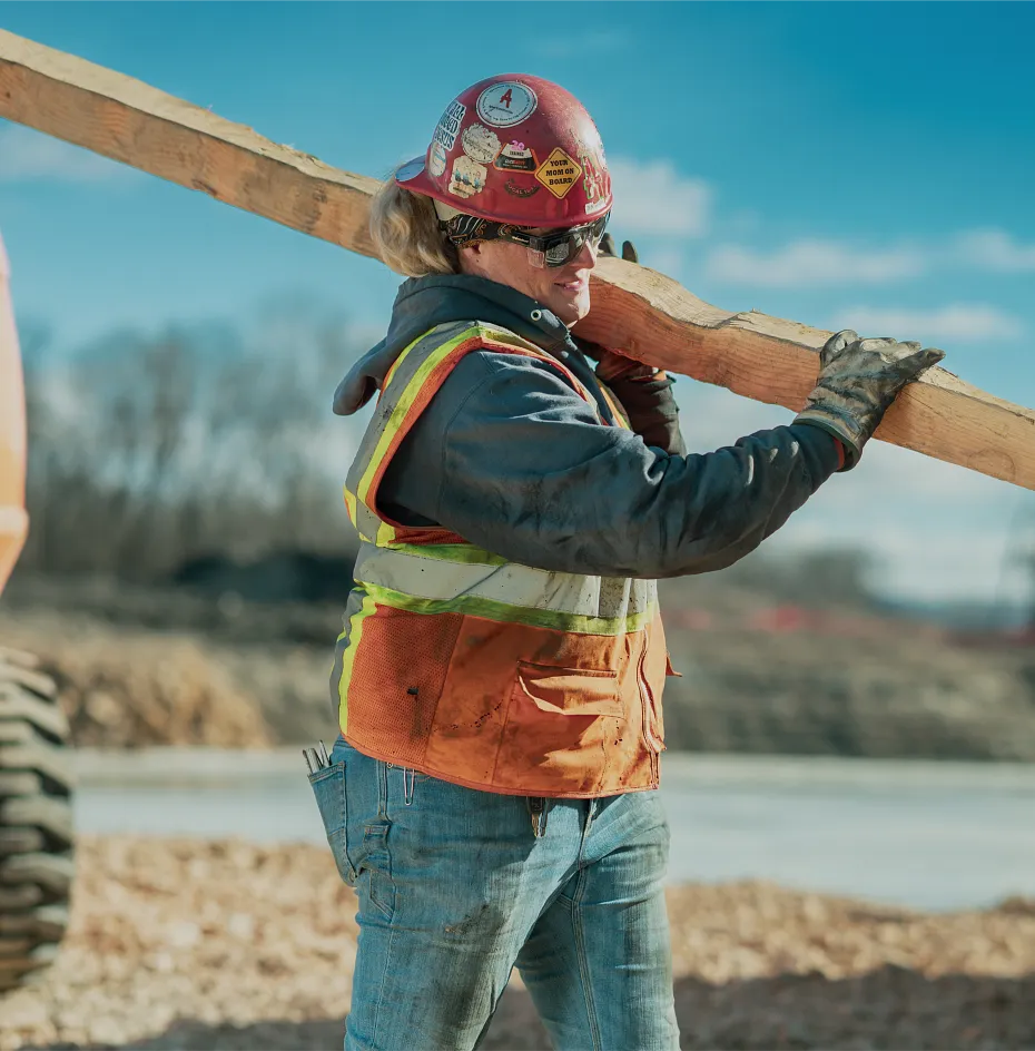 Woman on worksite carrying a wood board