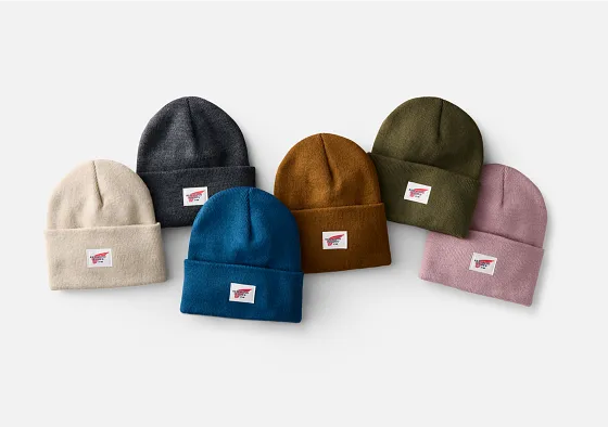 Overhead view of 5 beanie hats laying on a white surface