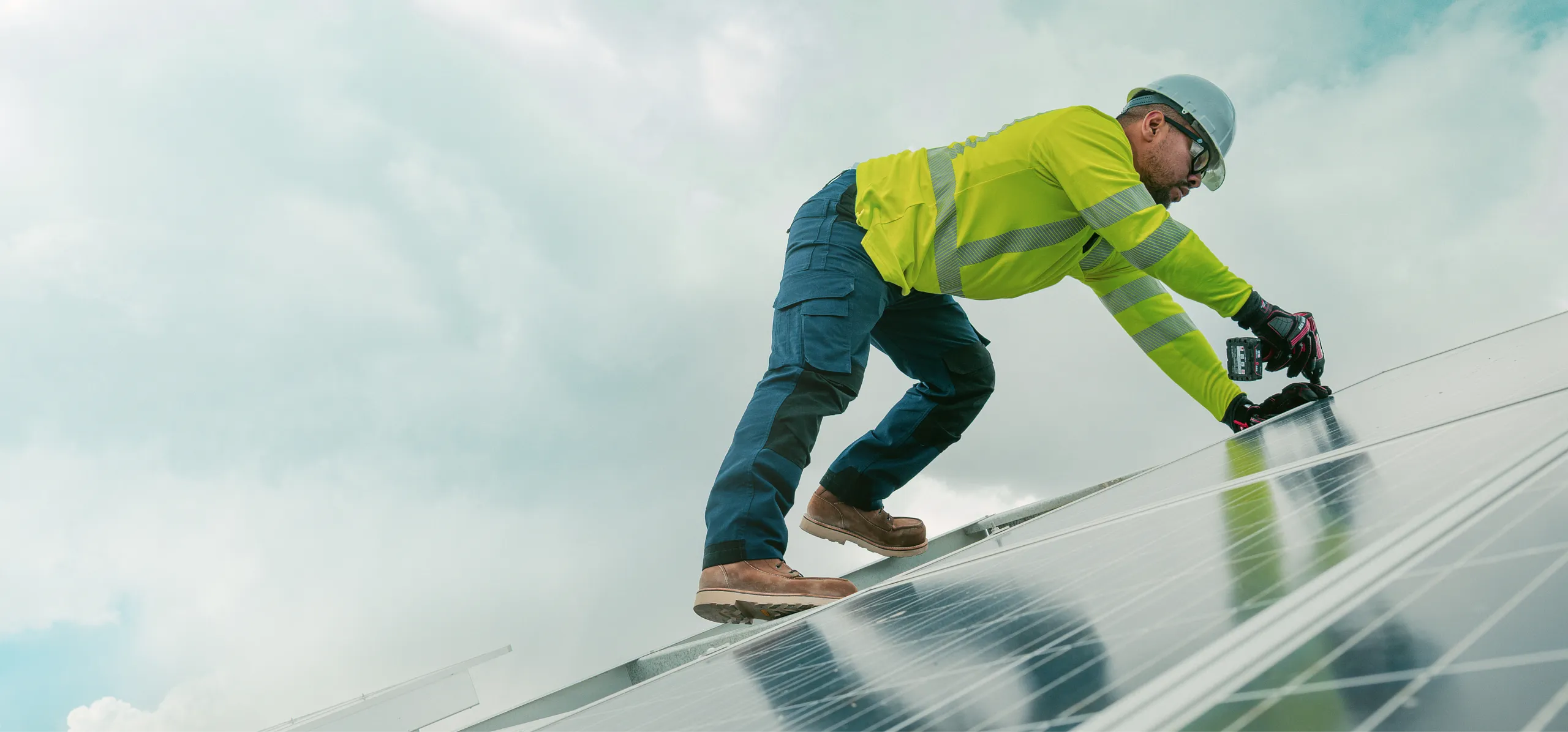 Upward view of a man in workwear screwing something into a solar panel 