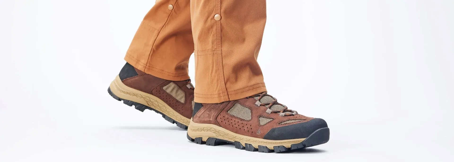 A closeup of a persons feet wearing Vasque Breeze hiking boots in a gray studio.