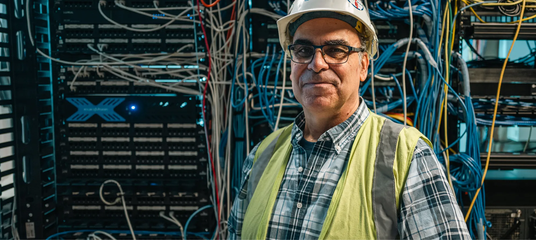 Closeup picture of Miguel A. Rueda wearing a hard hat standing next to a machine with wires