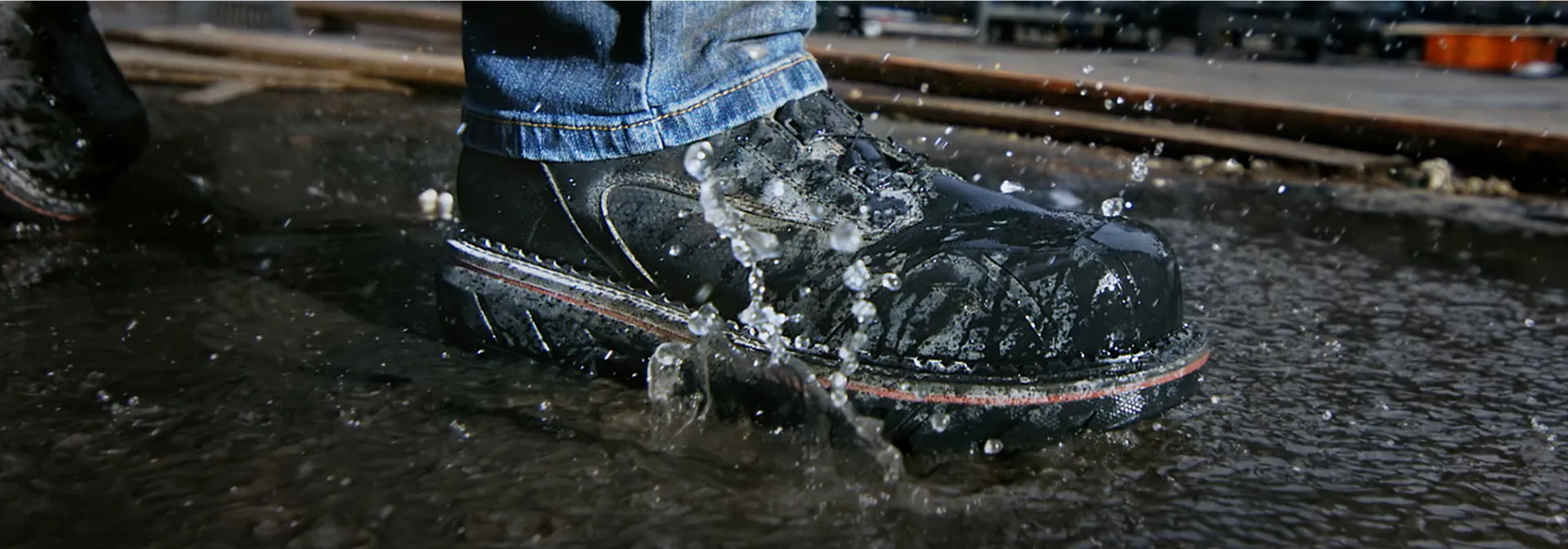 A Red Wing boot walking in water on a street 