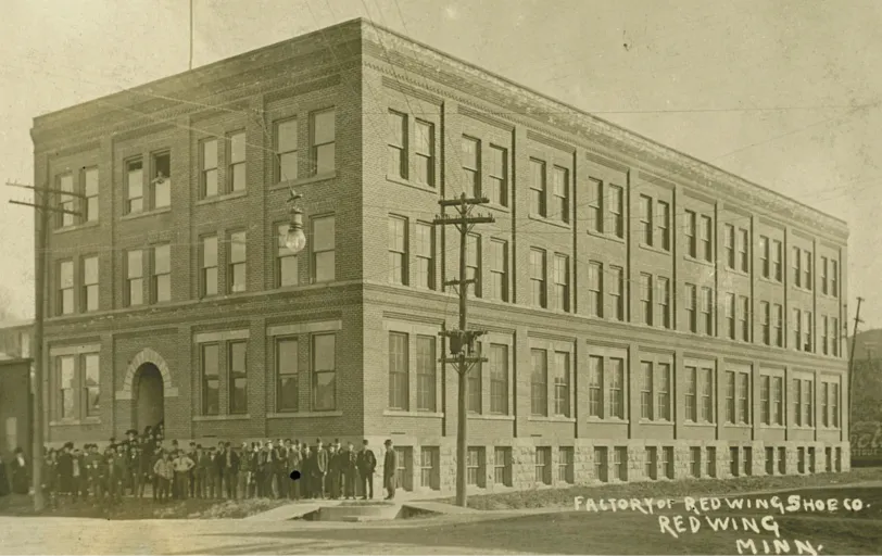 Historical photo of the Red Wing Shoe Factory with workers standing in front of the building 