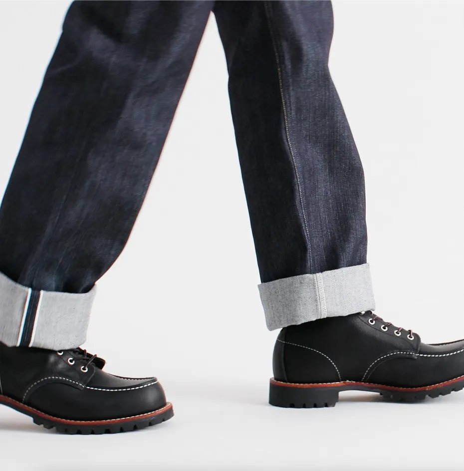 Close up of the bottom of a person's legs wearing jeans and boots against a white background