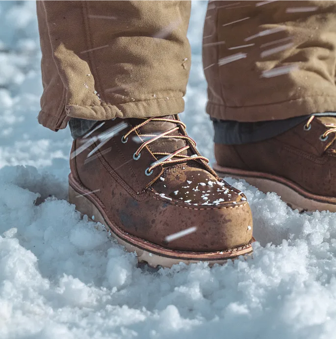 Close up of the bottom of a person's legs wearing boots, standing in snow