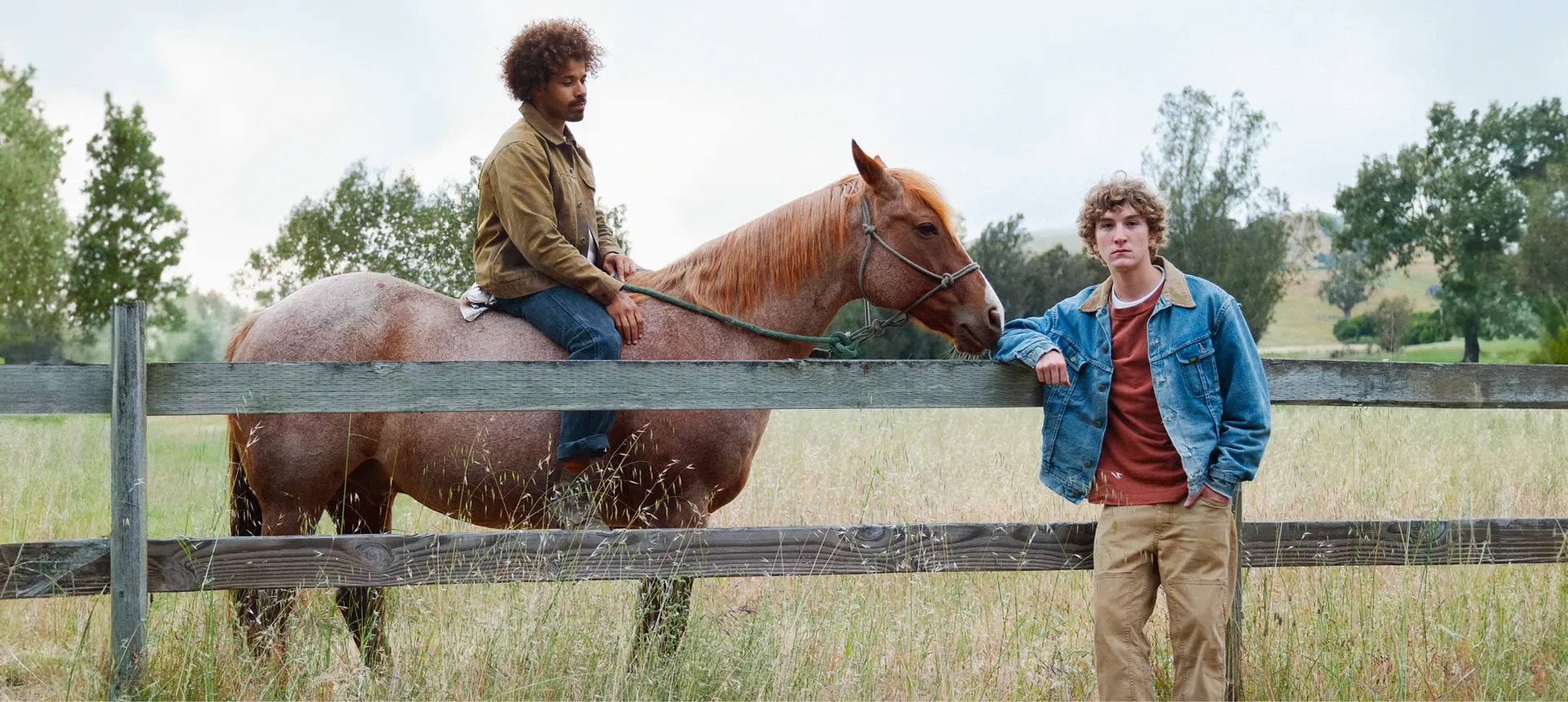 Brelen and Max, one sitting on a horse and one leaning on a fence in a field