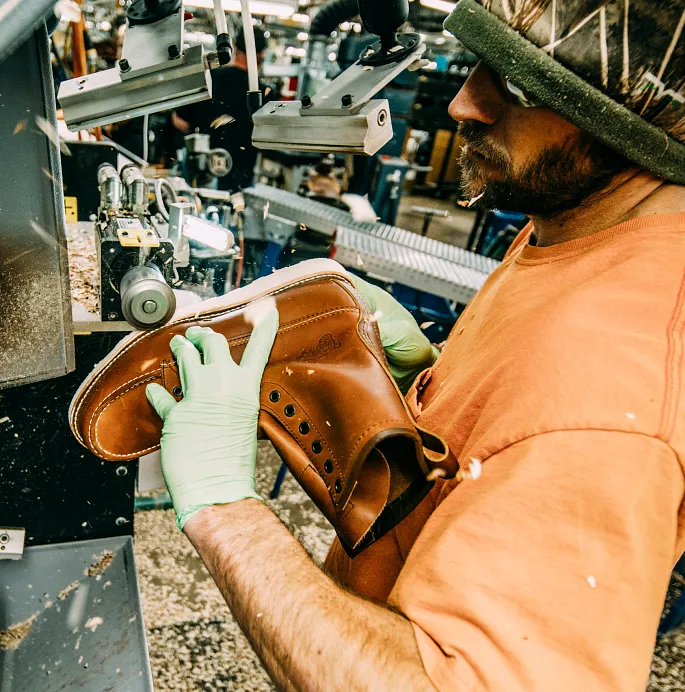 Close up of a man using a grinder on a boot in a workshop