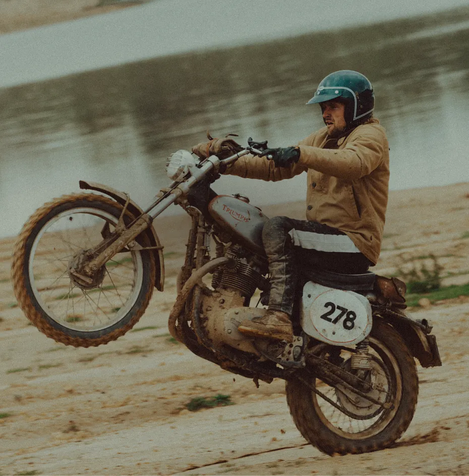 A man at a beach doing a wheelie on a motorcycle