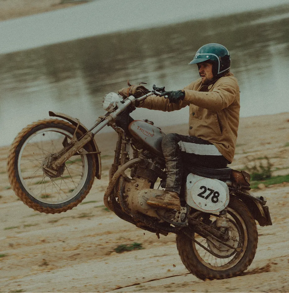 A man at a beach doing a wheelie on a motorcycle