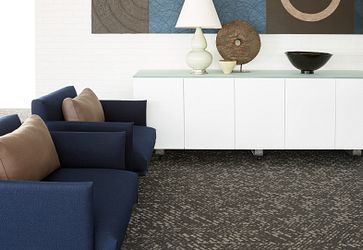 Modern office lounge with blue armchairs and a white cabinet, featuring a patterned commercial carpet tile in shades of gray, 9x36 inch dimensions