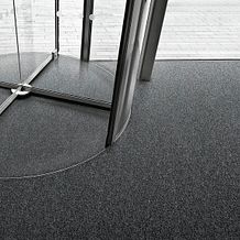 Entryway with dark gray commercial broadloom carpet and revolving glass door