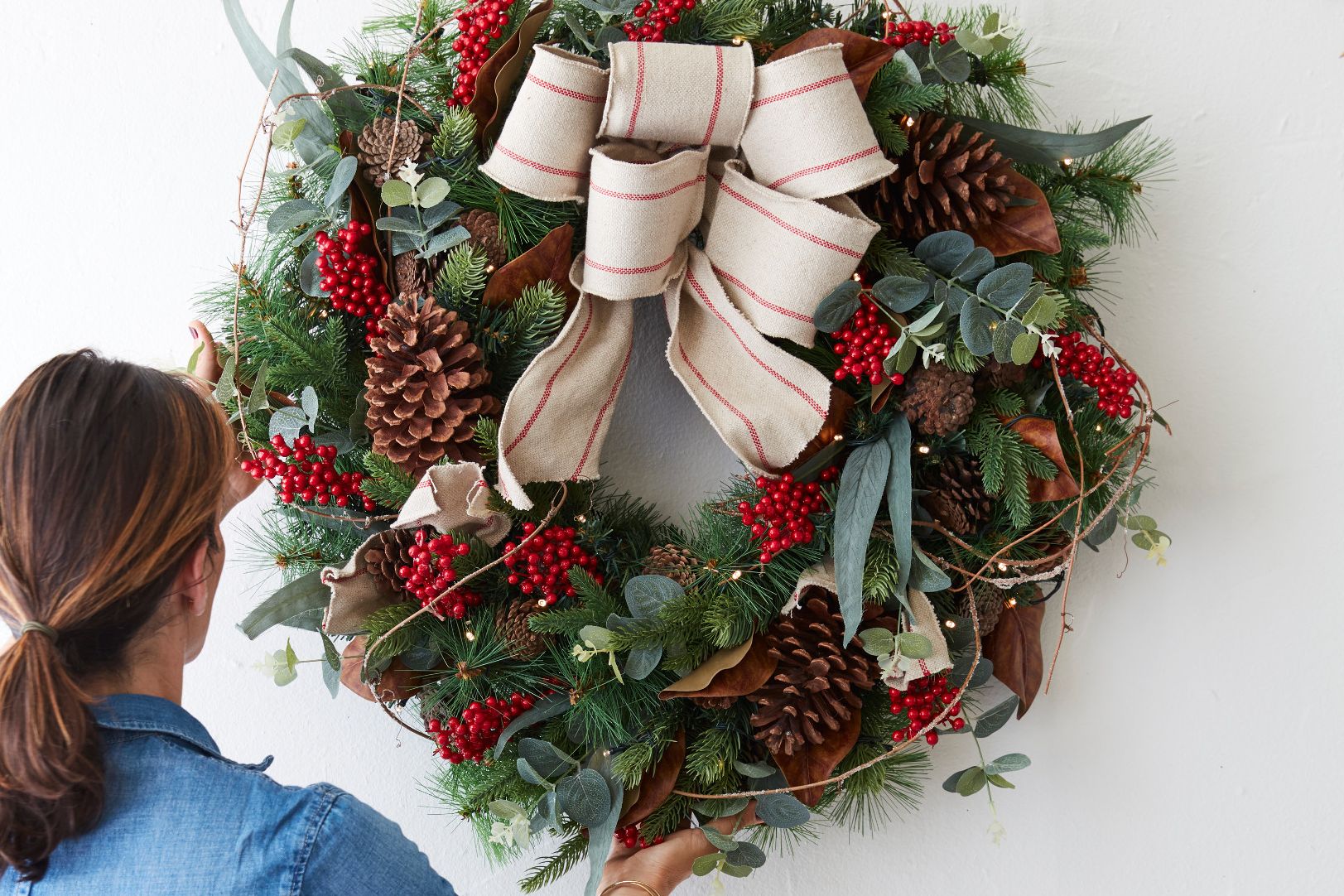 woman fixing a decorated artificial wreath on a white wall