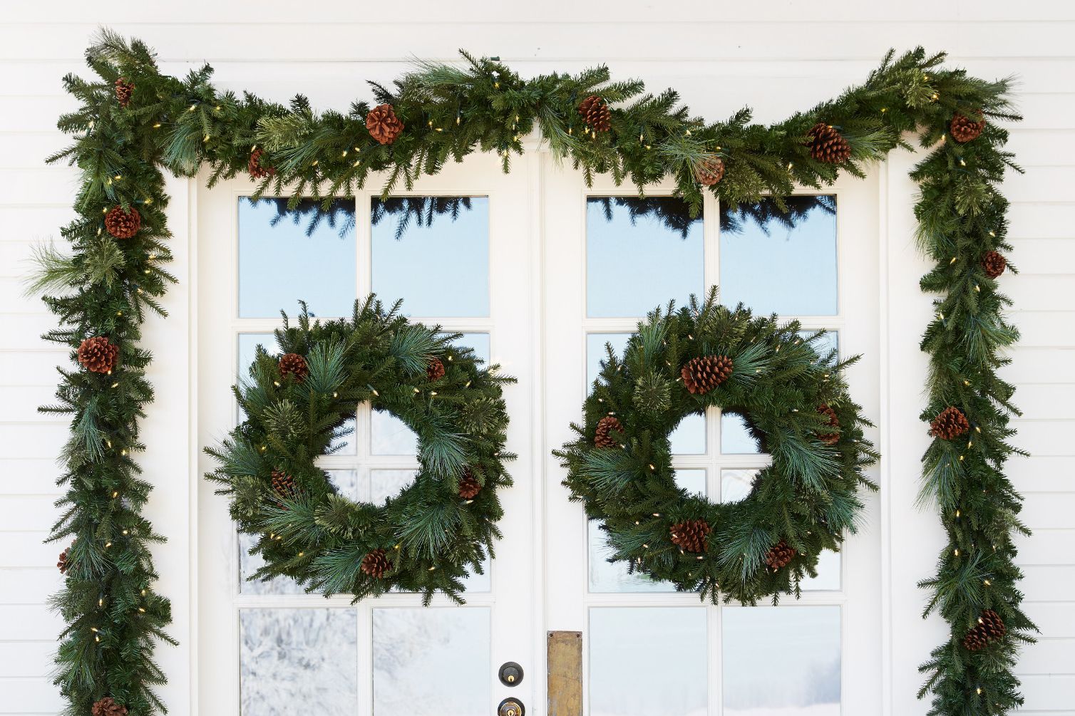 decorated greenery wreaths and garlands on a white front door