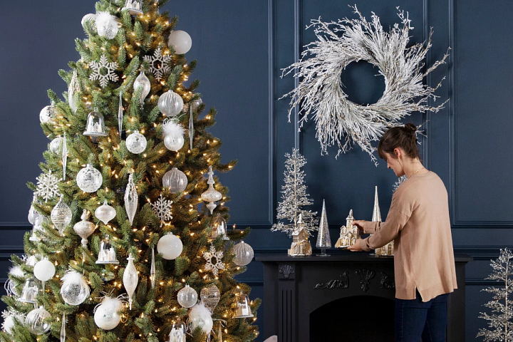 Woman fixing white and gold themed Christmas decorations in a blue room
