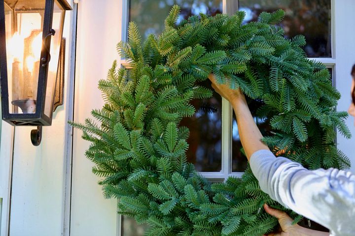 woman hanging an artificial wreath on a glass door