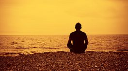 Man meditating on a beach at sunrise.