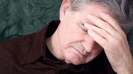 An older man looking despondent and holding his forehead