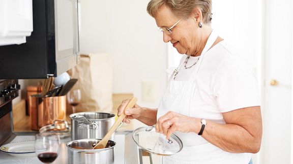 An older woman standing at a stove stirring a pot