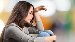 Woman sitting on the ground with her hand on her head experiencing a headache