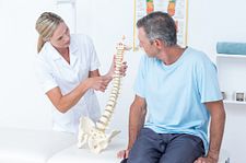 nurse pointing at model of spine next to male patient